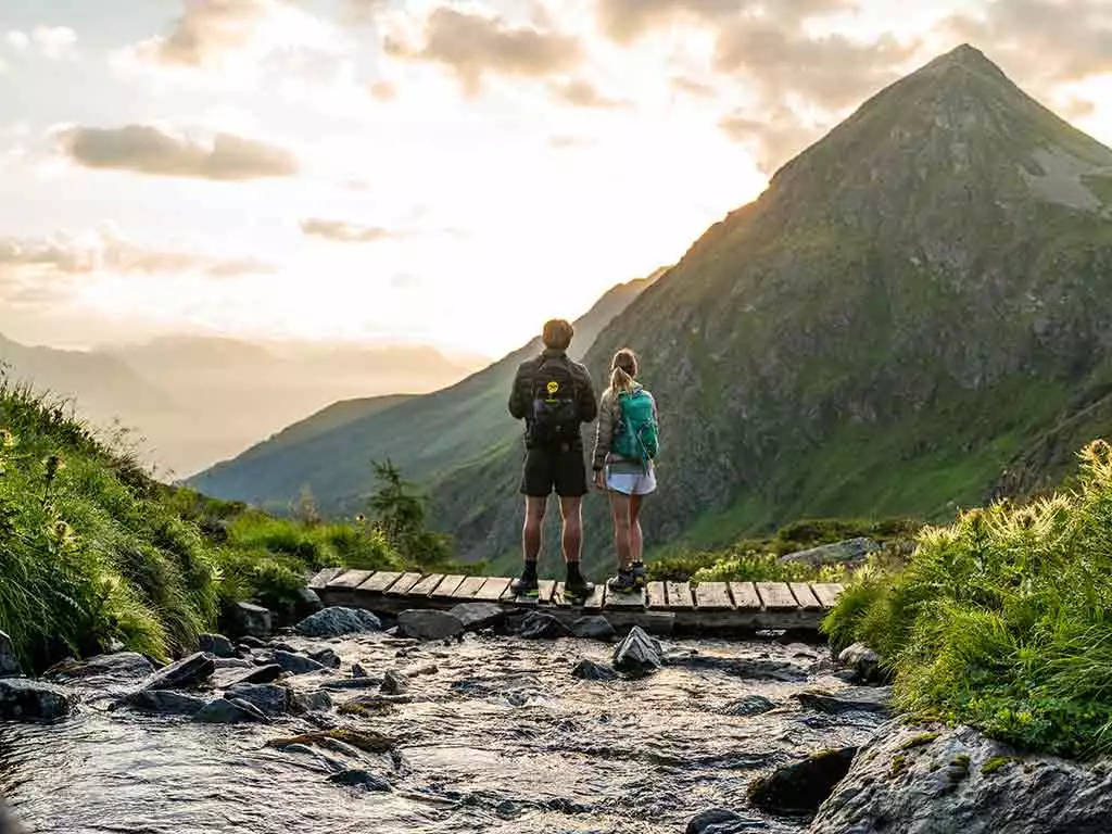 Wandern in Virgen in Osttirol, Bach mit Brücke und zwei Wanderer mit Blick über die Berge